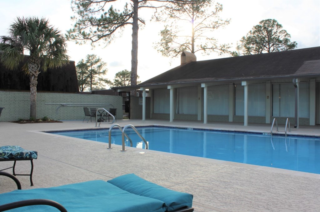 A pool with a bench and a chair with a house in the background.